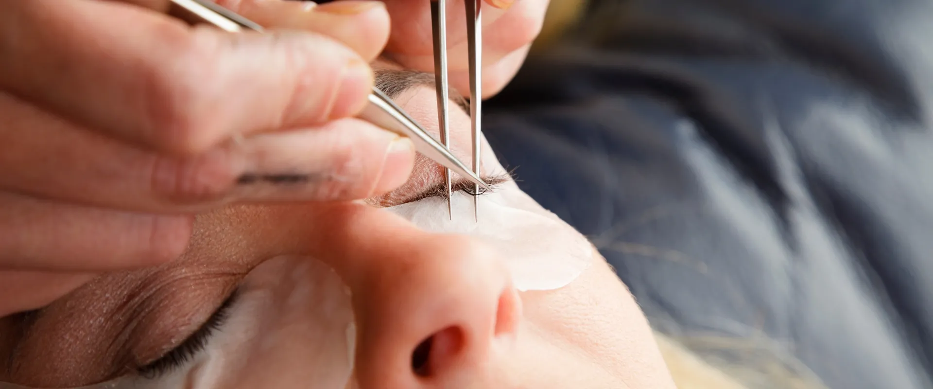 Close up of tweezers placing a lash extension onto a natural lash