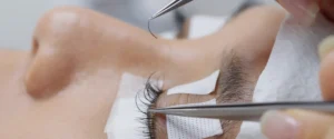 A lash artist bonding an extension onto an isolated natural lash with precision tweezers