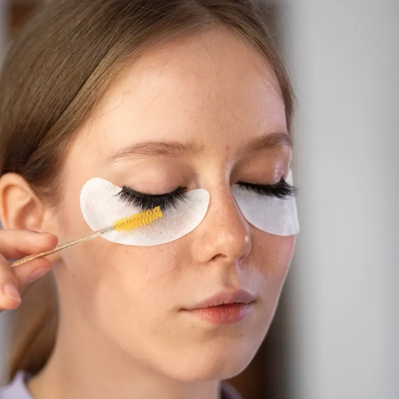 Brush-on strip lash adhesive being applied to a lash strip with a gold applicator